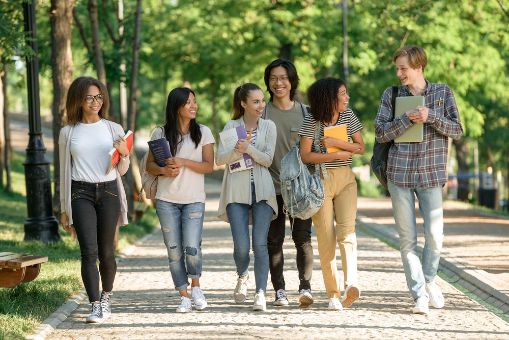 Image of multiethnic group of happy young students walking outdoors. Looking aside.