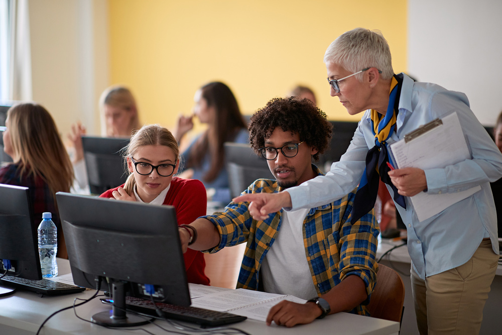 Female professor checking students work at an informatics lecture in the university computer classroom